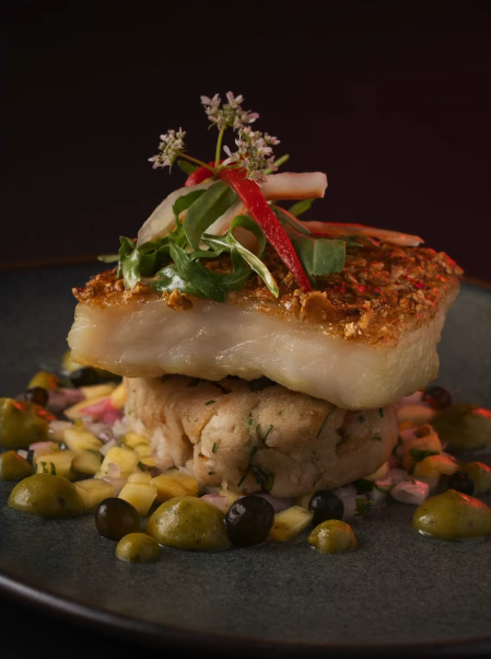 Pescado de pesca fresca con piel crocante servido sobre puré cremoso y vegetales frescos en Pescados Capitales, restaurante de cocina marina en Lima.