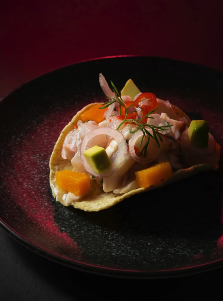 Taco crujiente relleno de ceviche peruano con palta, mango y cebolla roja servido en Pescados Capitales.